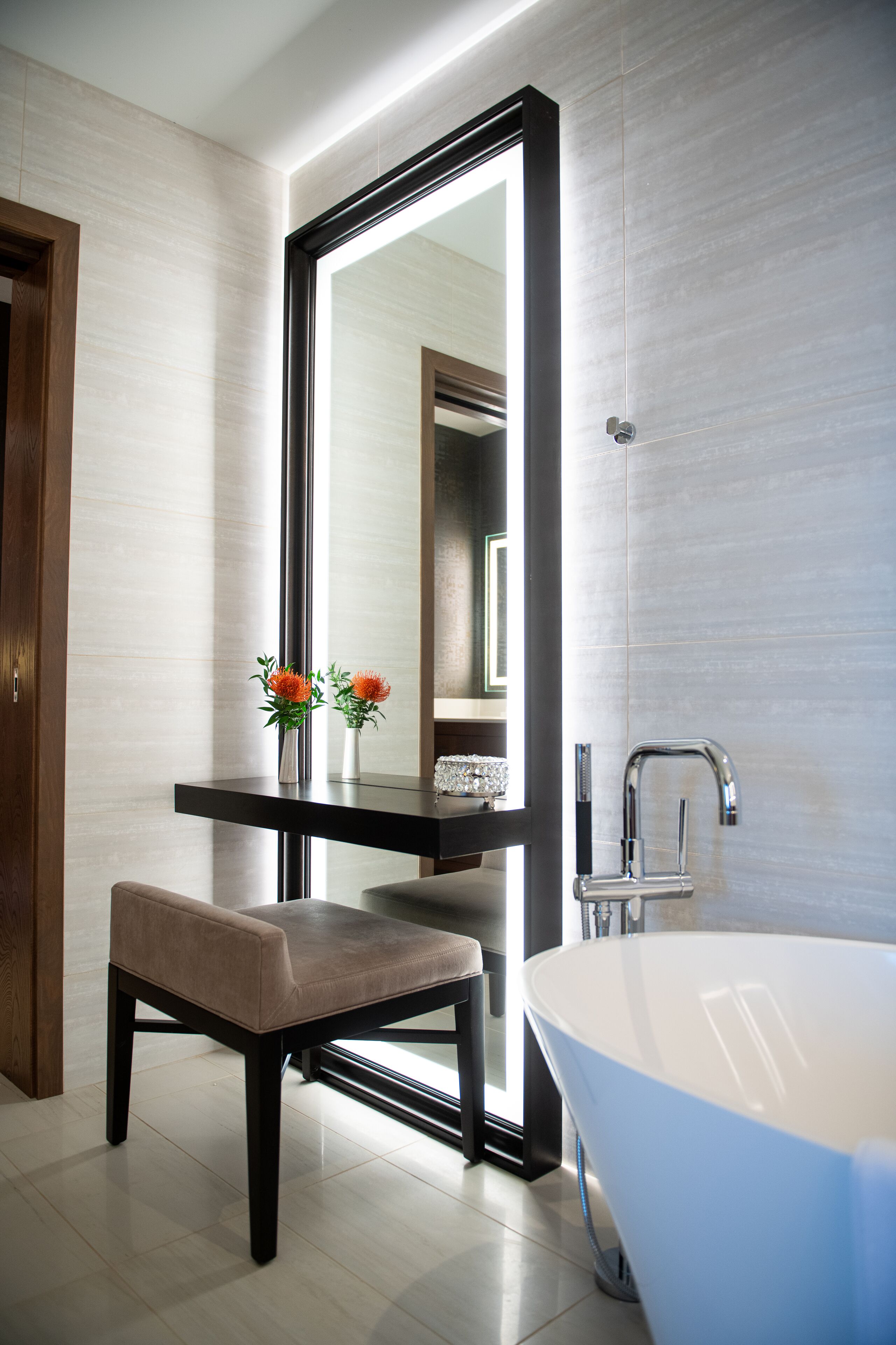 A modern bathroom with a large mirror, a bathtub, and a bench.