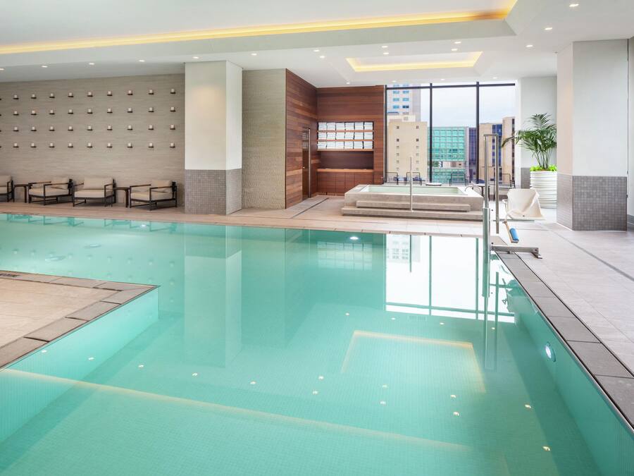 A hotel swimming pool with lounge chairs, a changing room, and a view of the cityscape.