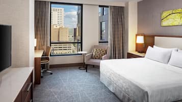 Een hotelkamer met een bed, een bureau, een stoel, een televisie en een raam met uitzicht op de stad.