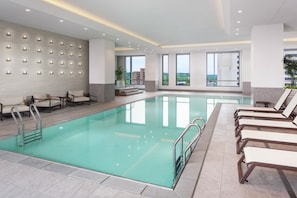 Una piscina interior moderna con agua cristalina, rodeada de tumbonas y una zona de estar con un revestimiento de pared estampado.