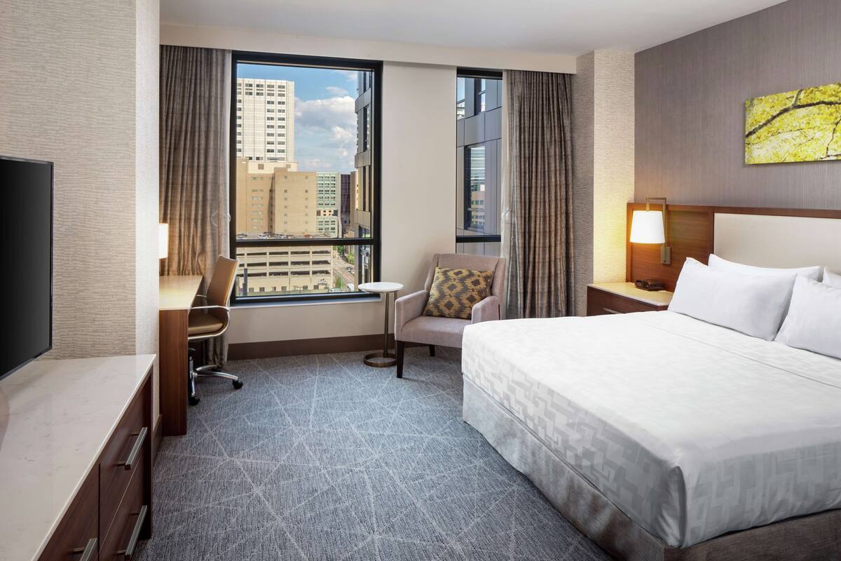 A hotel room with a large bed, a desk with a chair, a TV, and a window with curtains.