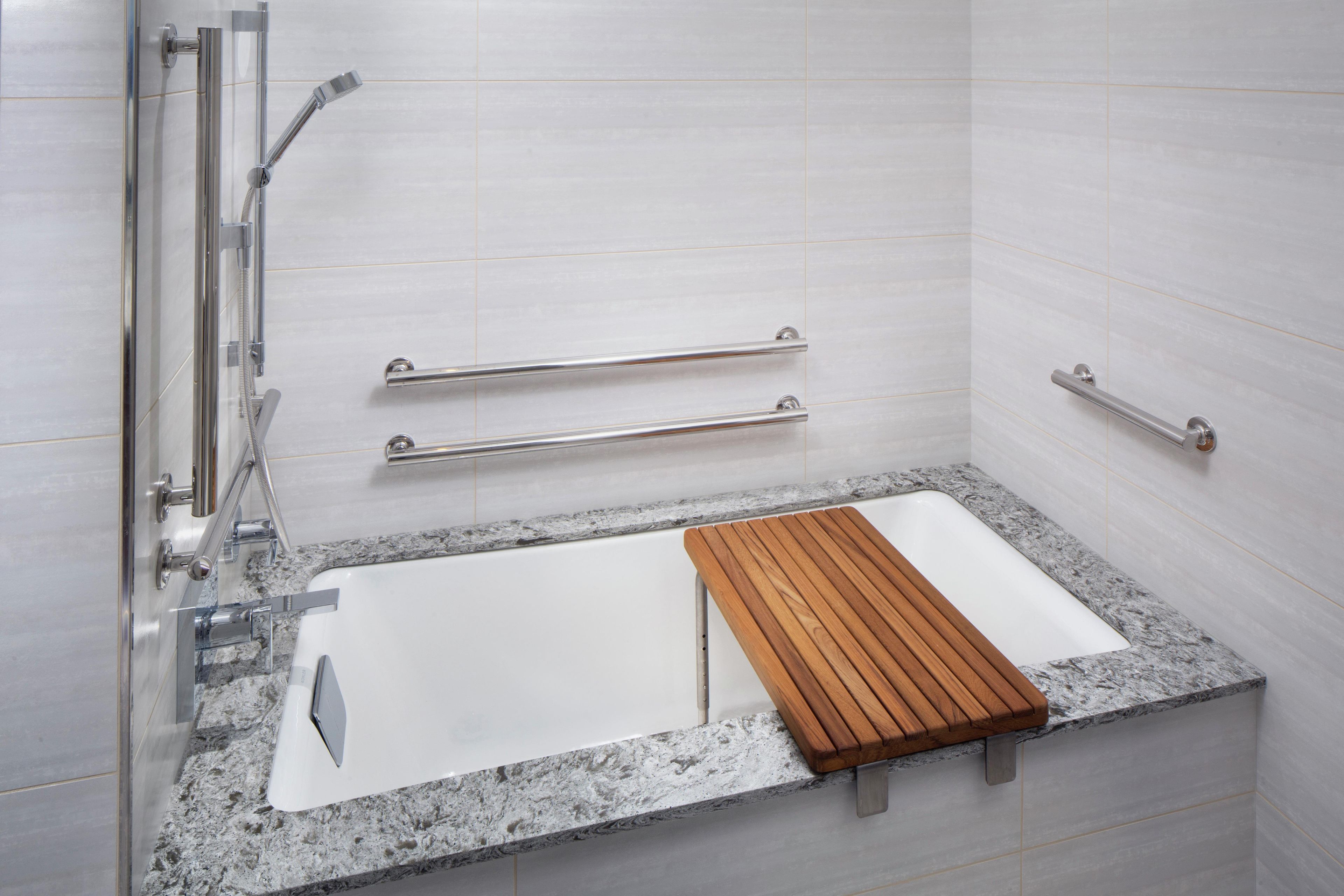 Un baño moderno con ducha a nivel, barras de apoyo y un tapete de baño de madera.