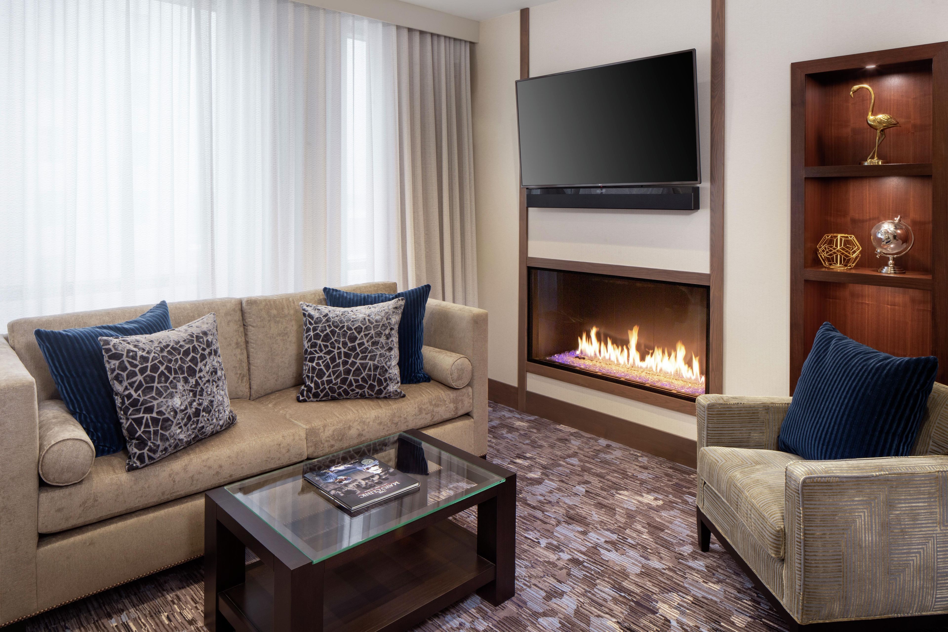 A living room with a sofa, armchair, flat-screen TV, fireplace, and decorative items.