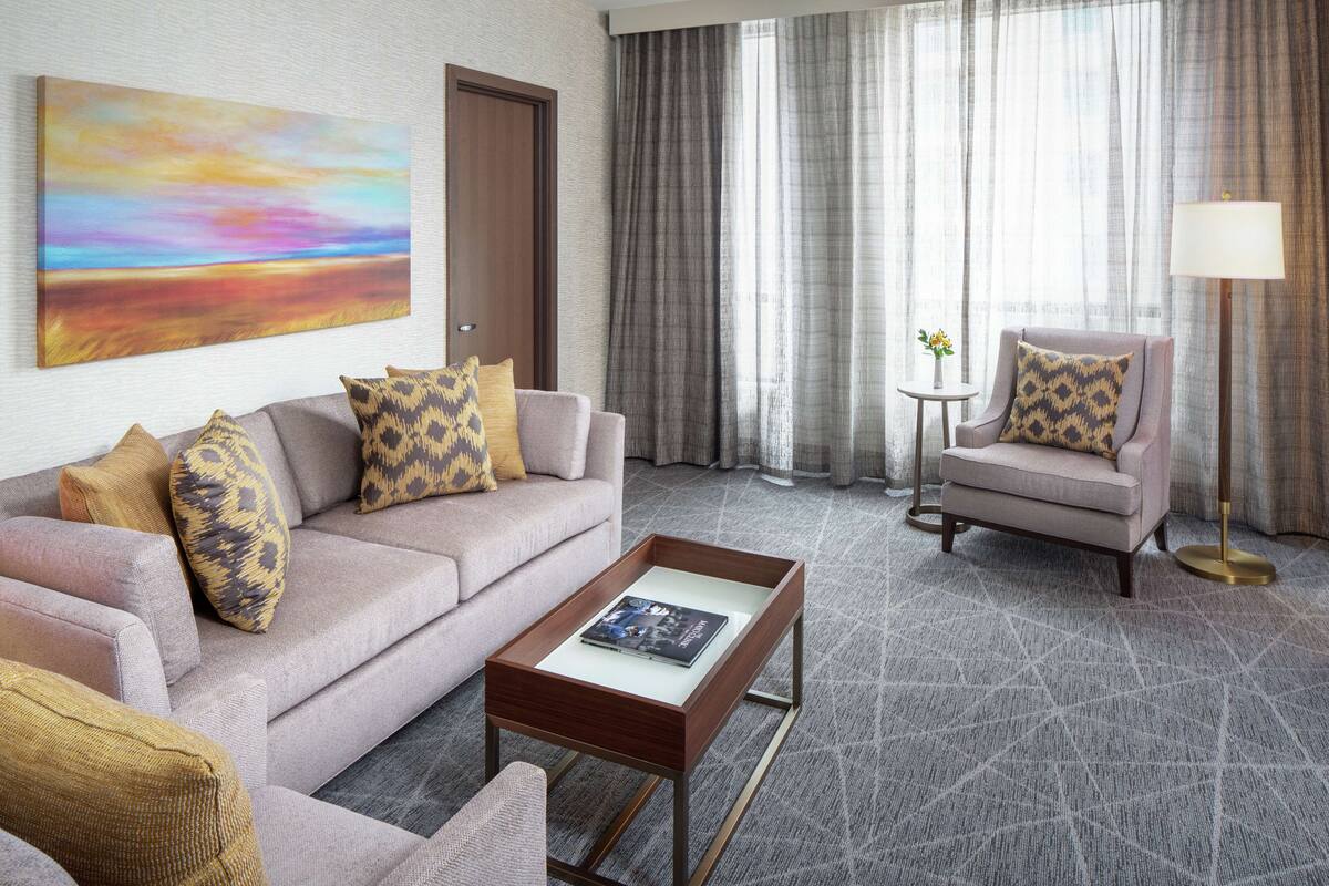 A modern living room with a sofa, armchair, coffee table, and a painting on the wall.