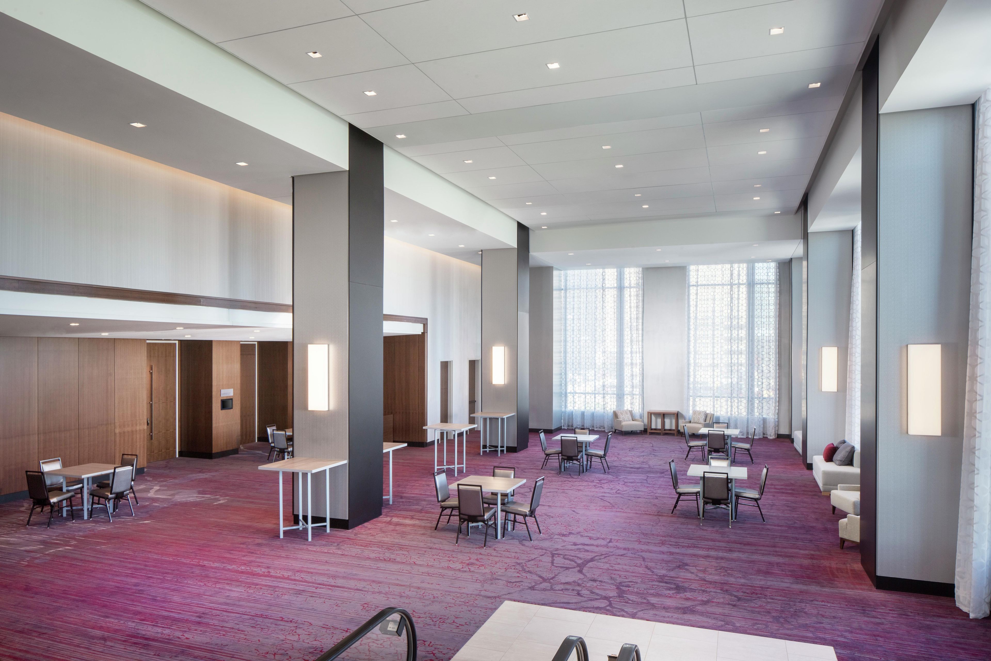 A spacious hotel lobby with multiple seating areas, a central column, and large windows allowing natural light.