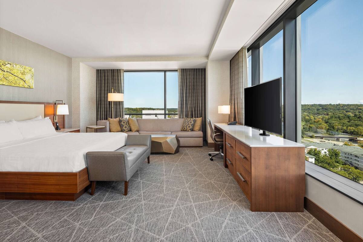 A hotel room with a large bed, a sofa, a desk, and a TV.