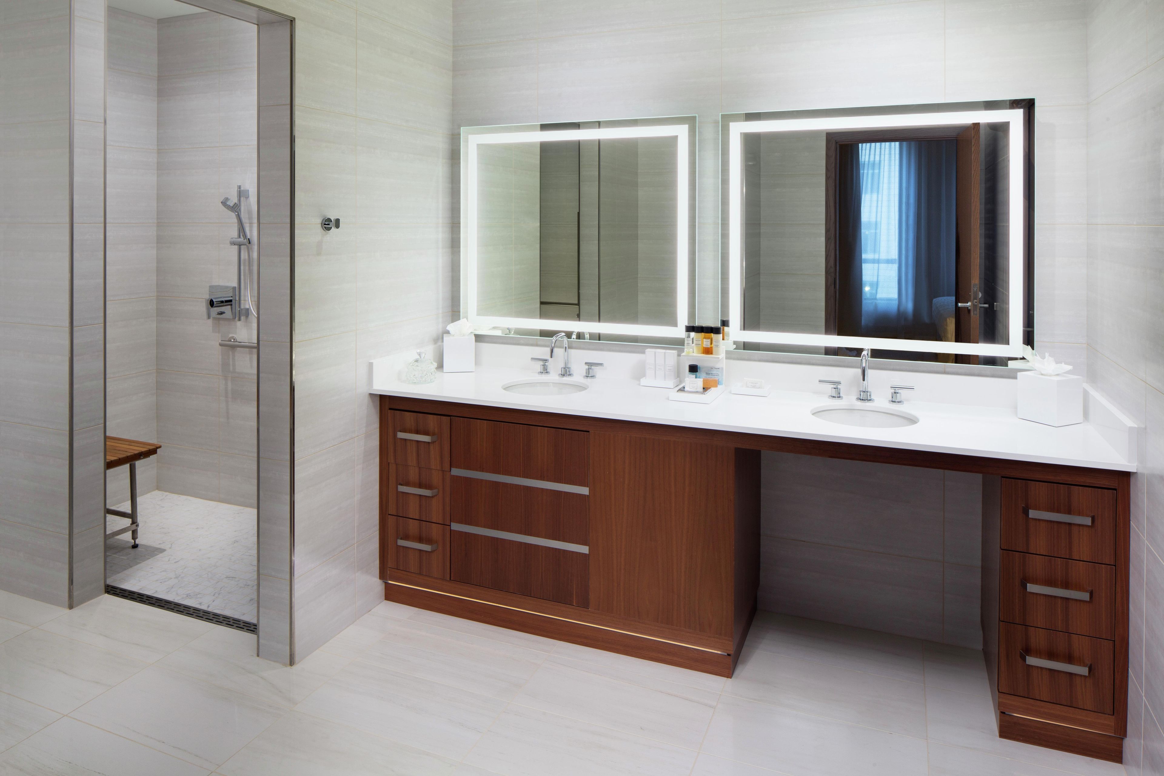 A modern bathroom with a glass shower enclosure, a double sink vanity with wooden cabinets, and a large mirror above the vanity.