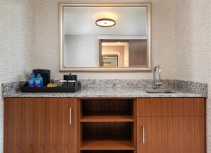 Une salle de bain avec un comptoir en granit, un lavabo, un miroir et une machine à café.