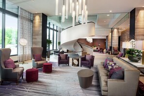 A spacious lobby with a curved staircase, comfortable seating areas, and large windows offering views of the outdoors. - Hilton Rochester Mayo Clinic Area (Rochester)