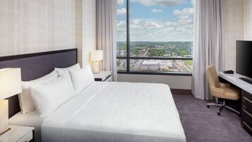 A hotel room with a large bed, a desk with a chair, a television, and a window with a city view.