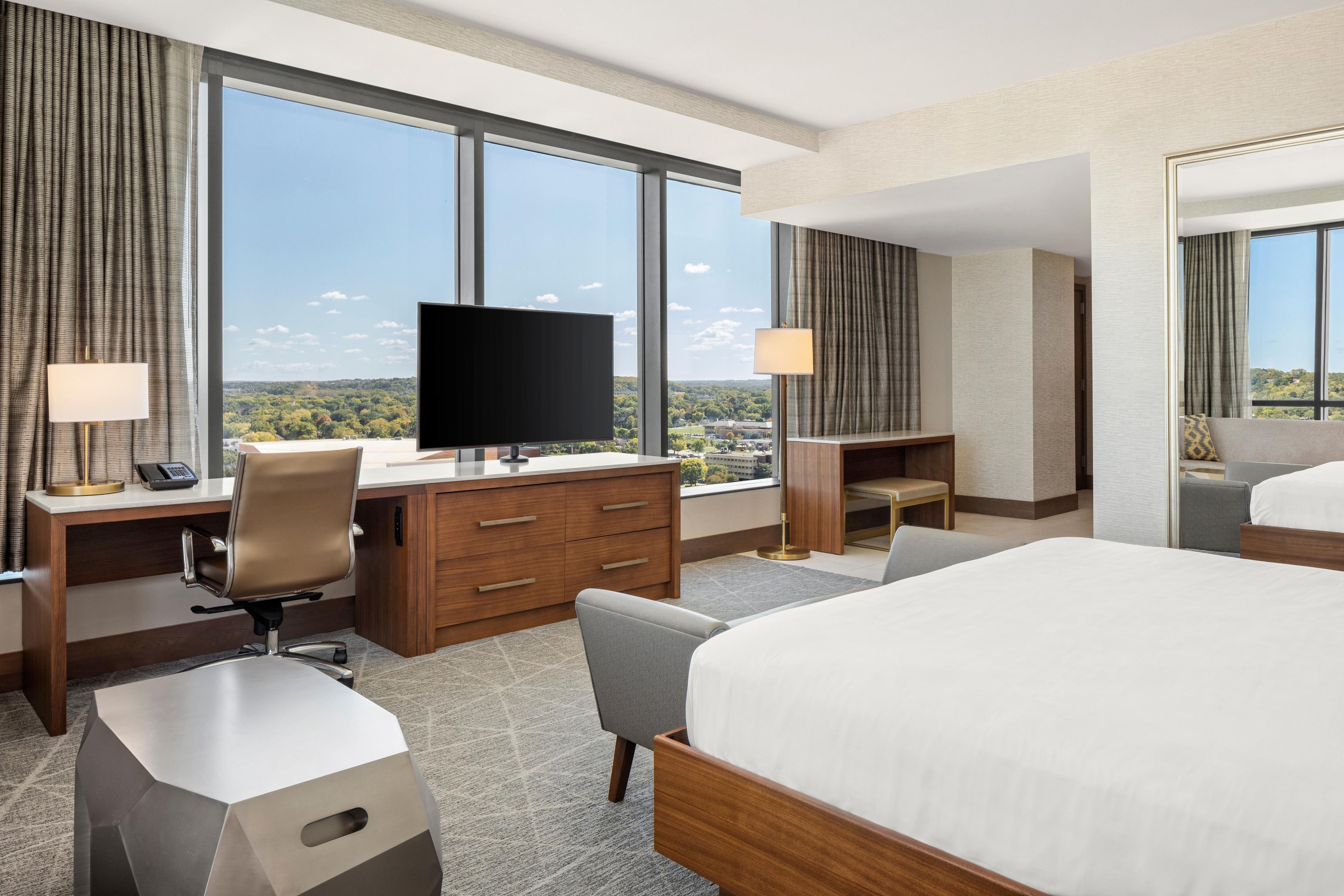 Une chambre d’hôtel avec un grand lit, un bureau doté d’un téléviseur à écran plat, une chaise, une commode et une vue sur le paysage urbain.