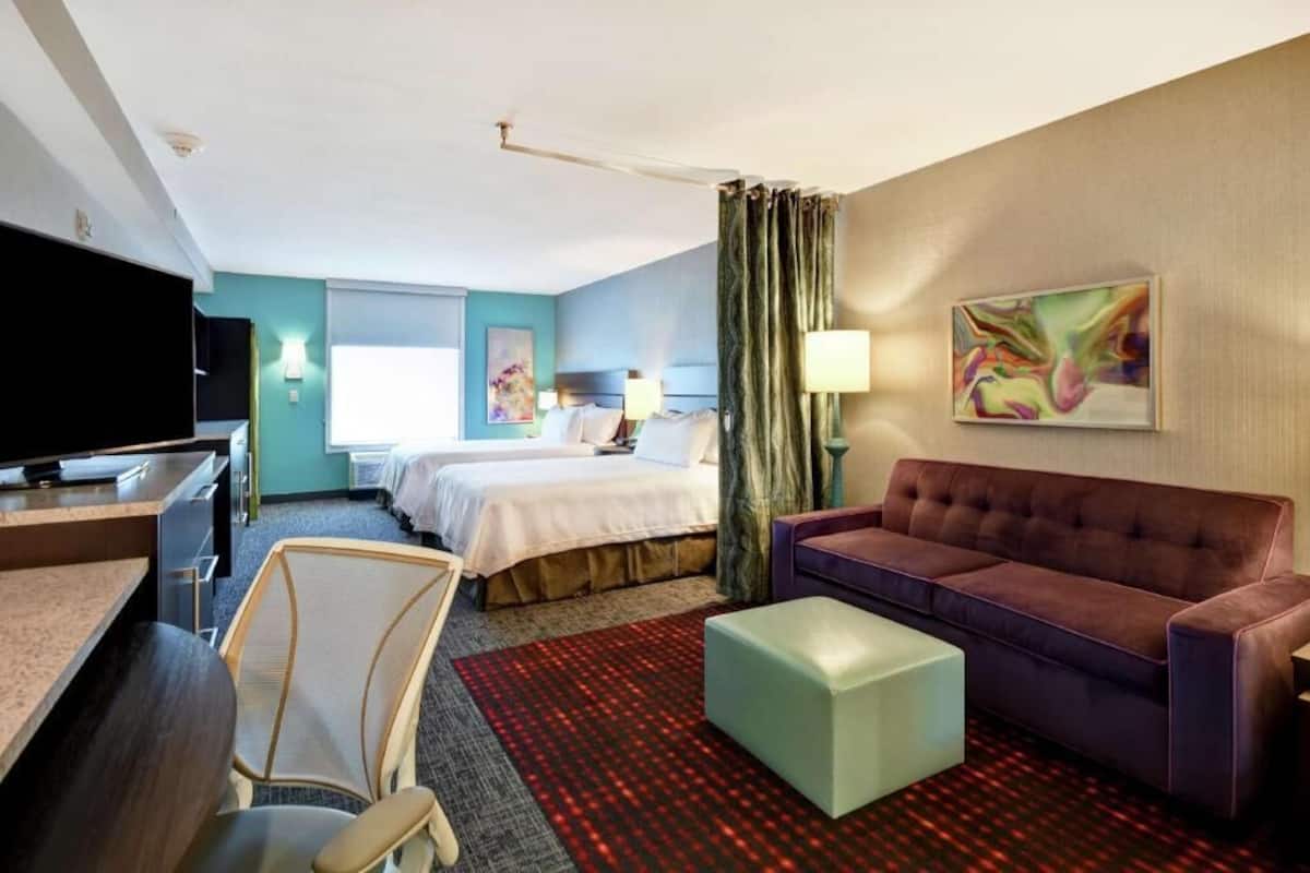 Hotellihuone, jossa on sänky, sohva, kirjoituspöytä, jossa on televisio, tuoli ja ikkuna.