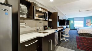 Een compacte hotelkamer met een kitchenette, een bed, een bureau en een raam met uitzicht.