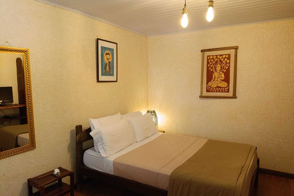 Un dormitorio con una cama, una mesita de noche, un espejo y dos cuadros colgados en la pared.