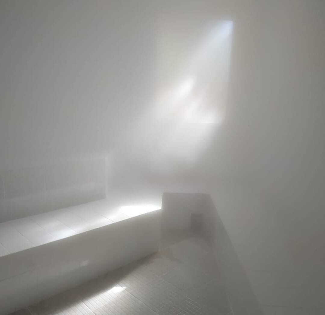 A room with a large window allowing natural light to enter. There is a visible staircase leading to an upper level.