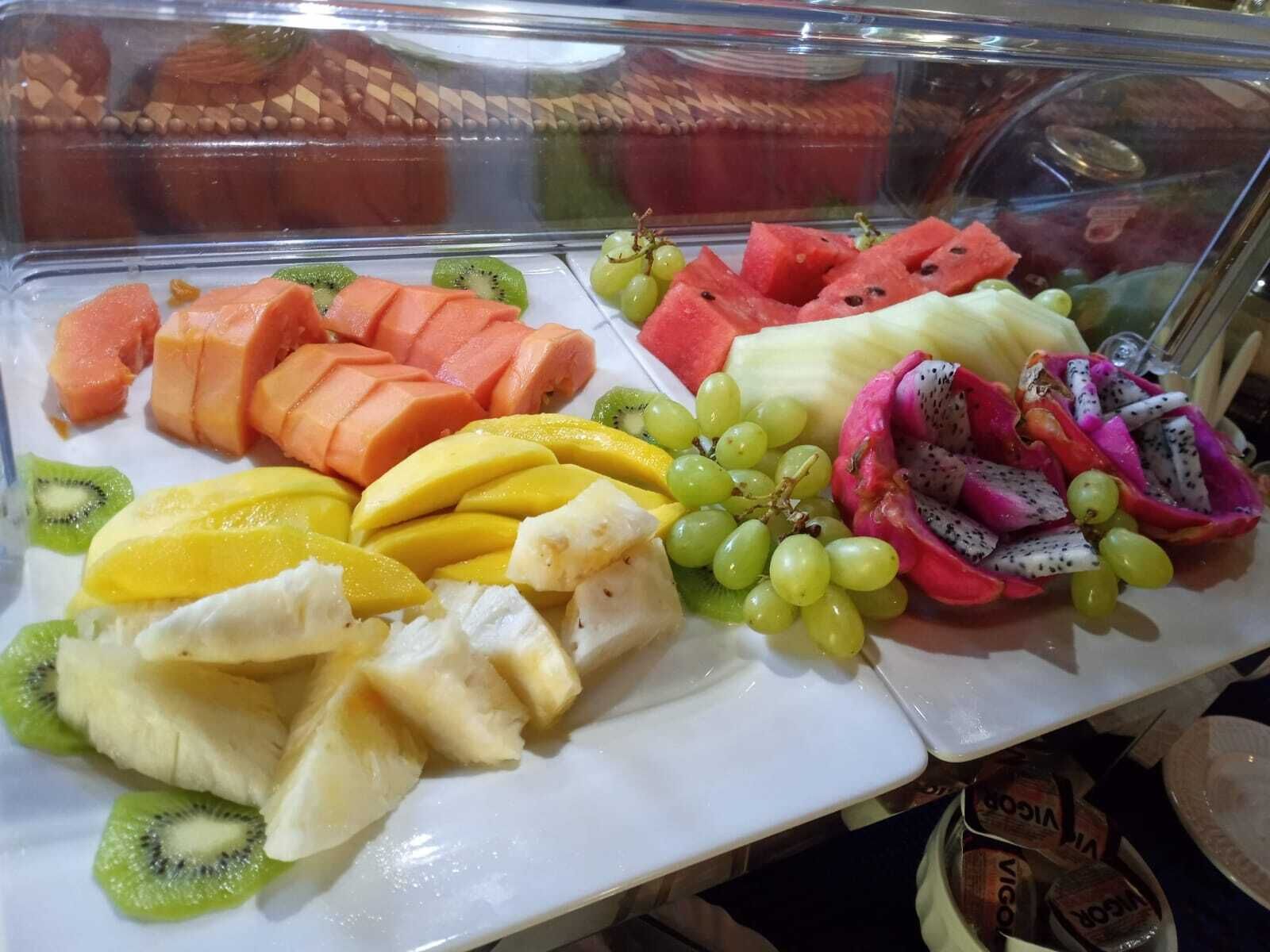 A fruit display with various fruits including watermelon, grapes, mango, kiwi, dragon fruit, and cantaloupe.