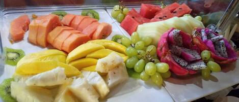 A fruit display with various fruits including watermelon, grapes, mango, kiwi, dragon fruit, and cantaloupe.