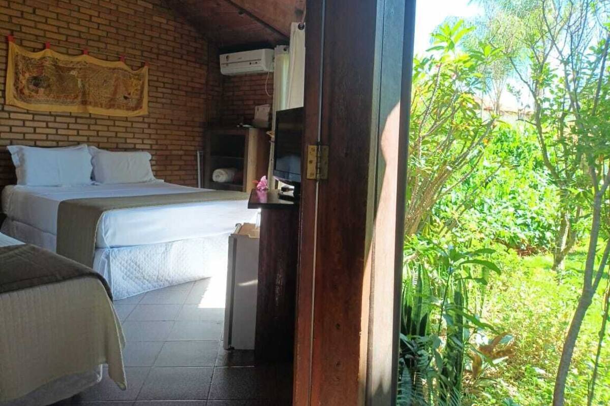 Habitación con dos camas, una pared de ladrillo y vistas al exterior con vegetación.