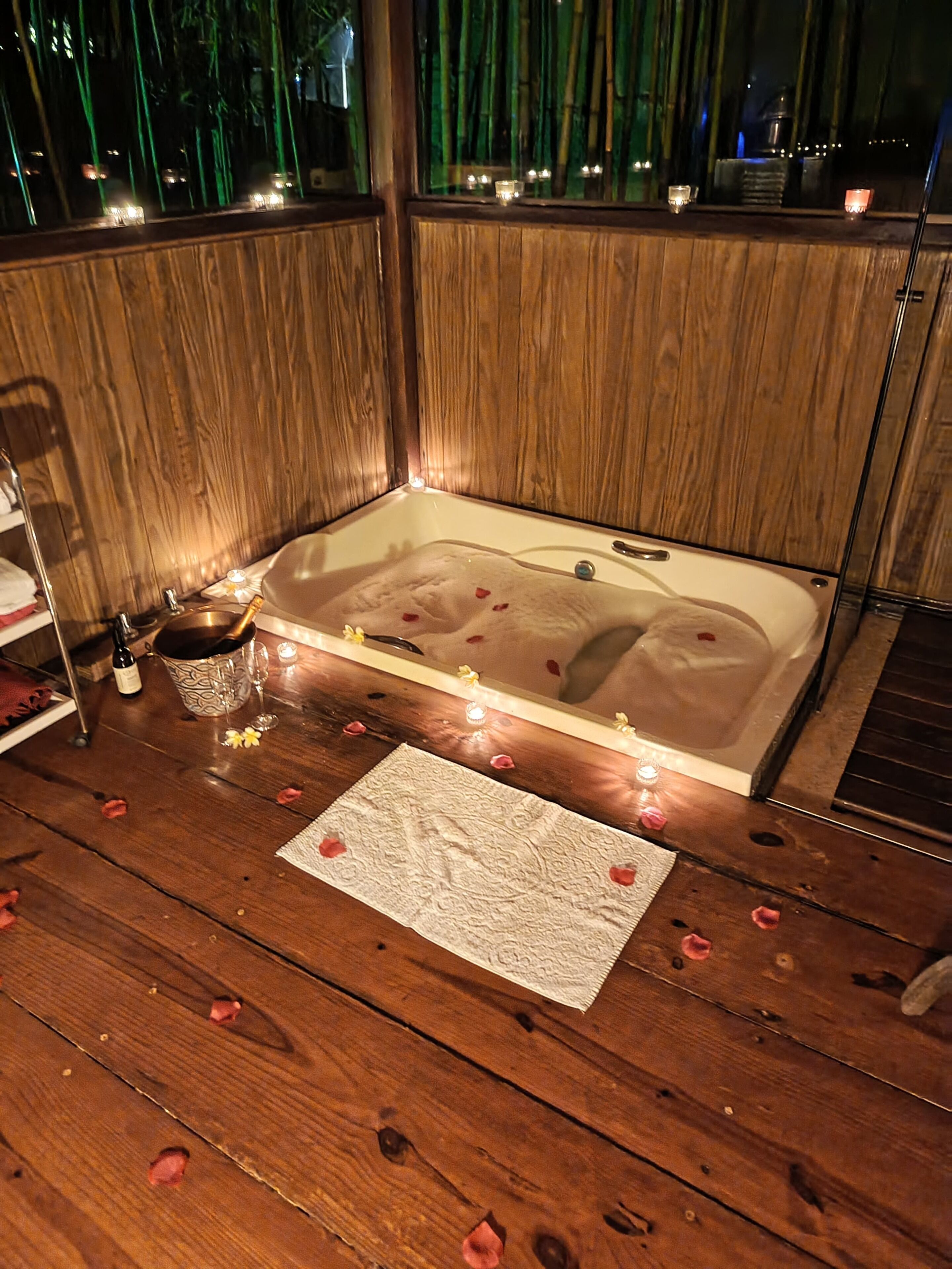 A wooden room with a bathtub, candles, and rose petals on the floor.