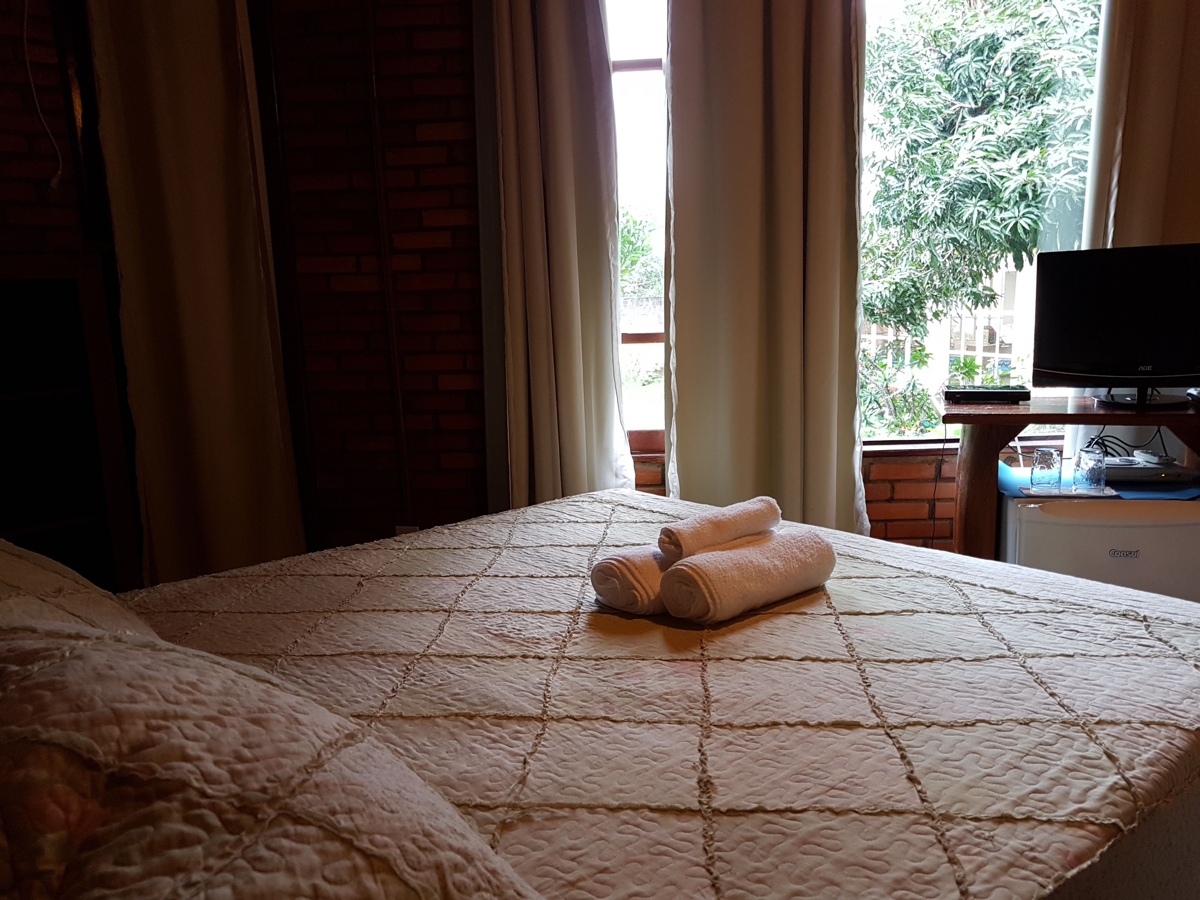 Quarto de hotel com cama, televisão e janela com cortinas.