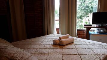 Quarto de hotel com cama, televisão e janela com cortinas.