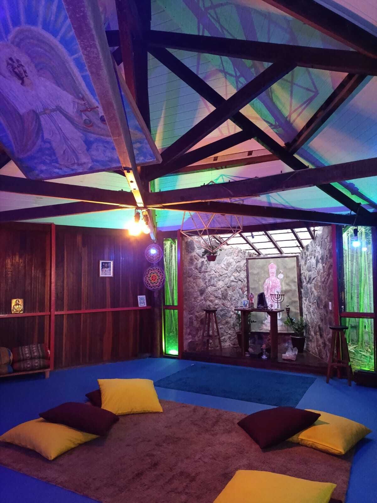 A room with a high ceiling, wooden beams, a stone wall, and a small altar with religious items.