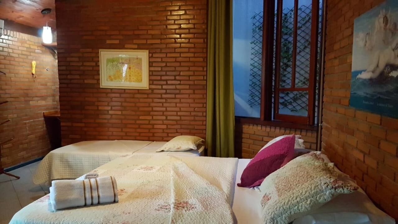A room with two beds, a brick wall, a framed picture, and a window with a view.