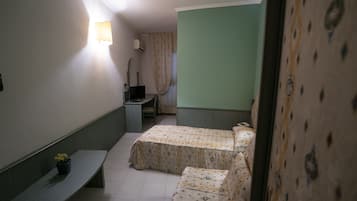 Una habitación pequeña y estrecha con dos camas, un banco, un escritorio y una lámpara fijada a la pared.