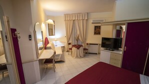 Habitación de hotel con una cama, un escritorio, una silla, un televisor y una mesita de noche con lámpara.