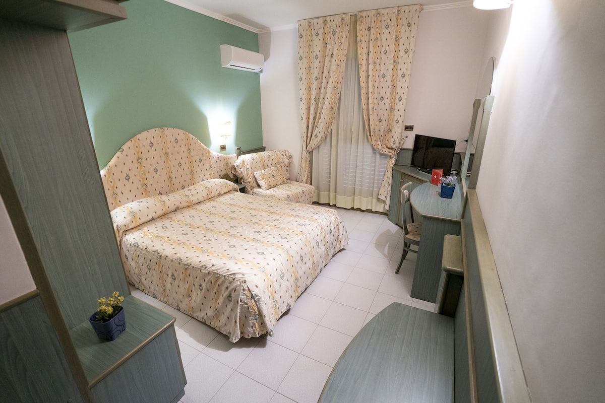 Ein Schlafzimmer mit Bett, Nachttisch, Spiegel und Vorhängen.