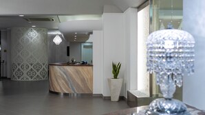 Una moderna recepción con mostrador de mármol, una planta decorativa y un candelabro de cristal.