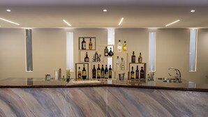 Una zona de bar moderna con encimera de mármol, varias botellas de licores y un lavamanos de acero inoxidable.