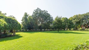 Um parque bem cuidado, com gramado, árvores e um banco de pedra.