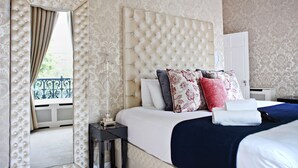 A hotel room with a tufted headboard, a large mirror with a decorative frame, a bedside table with a lamp, and a neatly made bed with multiple pillows. - The Bono Suite- hiphipstay (Dublin)