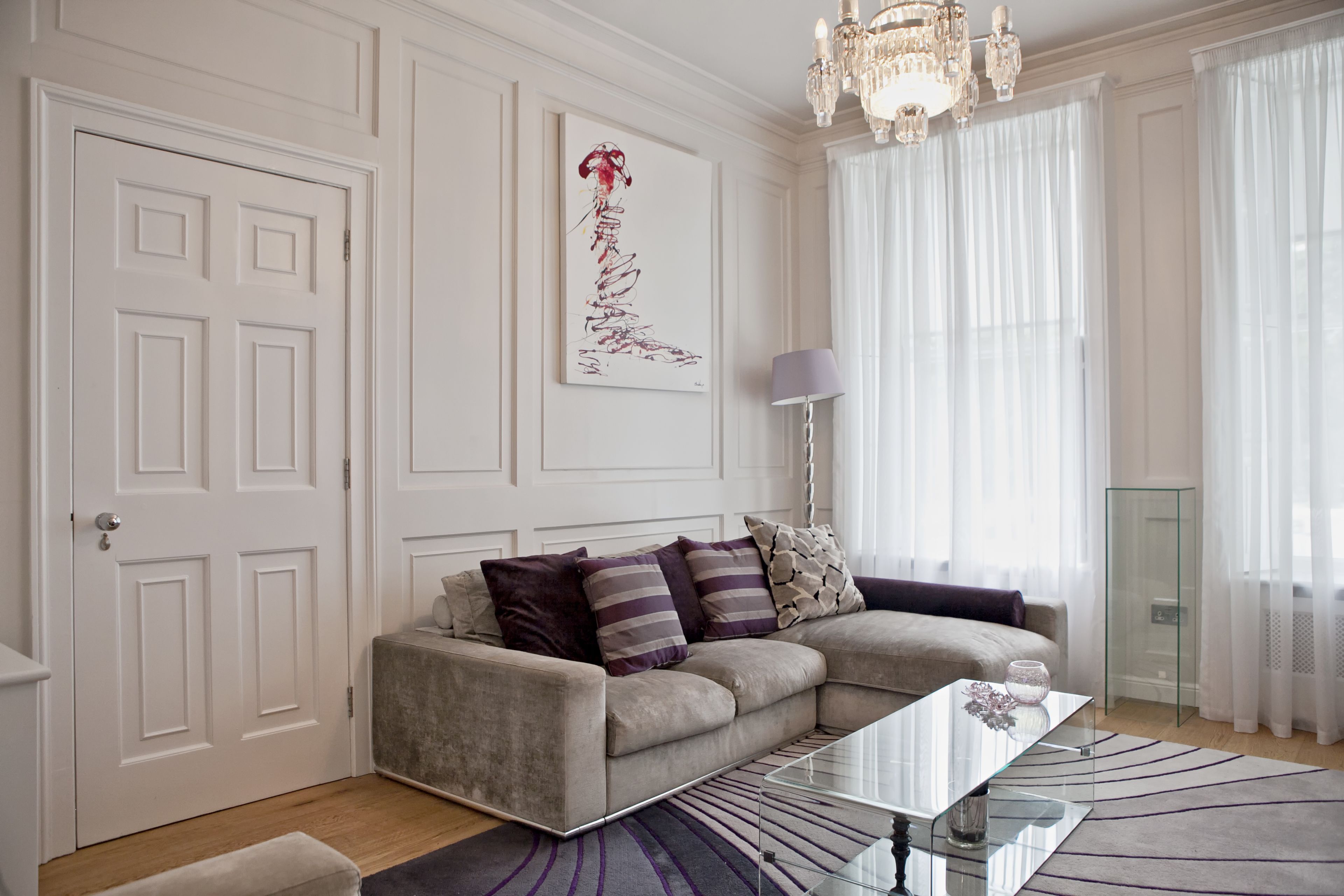 A modern living room with a beige sectional sofa, a glass coffee table, and a large abstract painting on the wall.