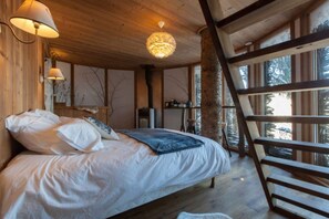 Un dormitorio rústico con cabaña de madera, una cama, una escalera y un ventanal grande con vistas a los árboles.