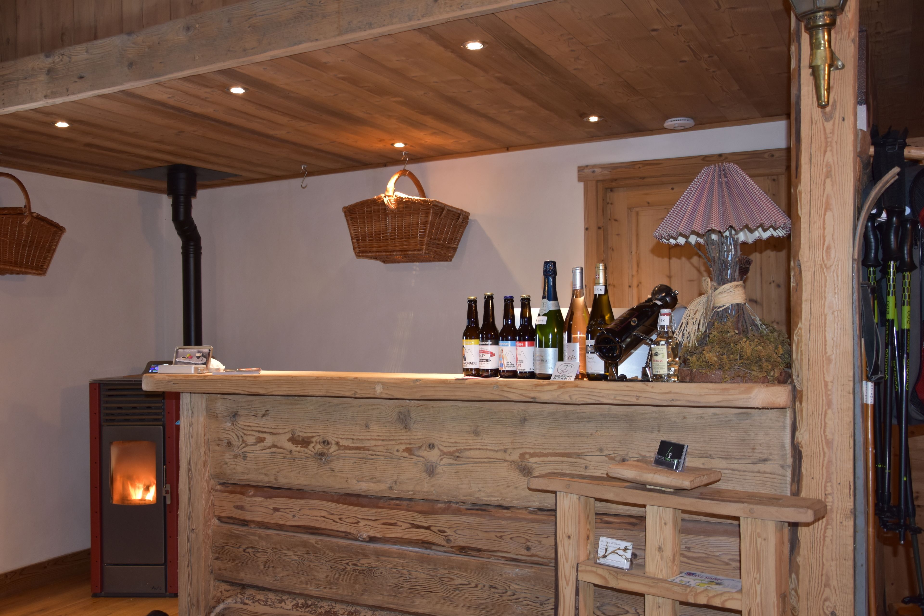 A rustic wooden bar area with a wood-burning stove, bottles of wine, and a small bench.