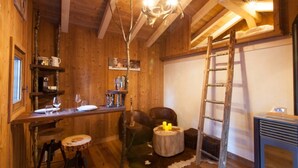 A rustic wooden interior with a dining area, a wooden ladder, and a fireplace.