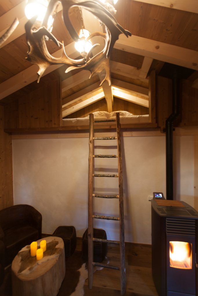 Una habitación acogedora con techo de madera, una escalera, un estufa de leña y un pequeño rincón de estar con cojines.