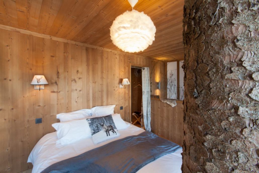 A wooden room with a bed, a stone wall, and a hanging light fixture.