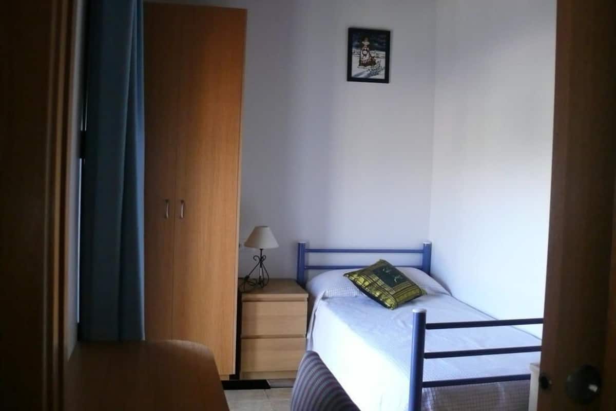 A bedroom with a bed, a nightstand, a lamp, and a wardrobe.