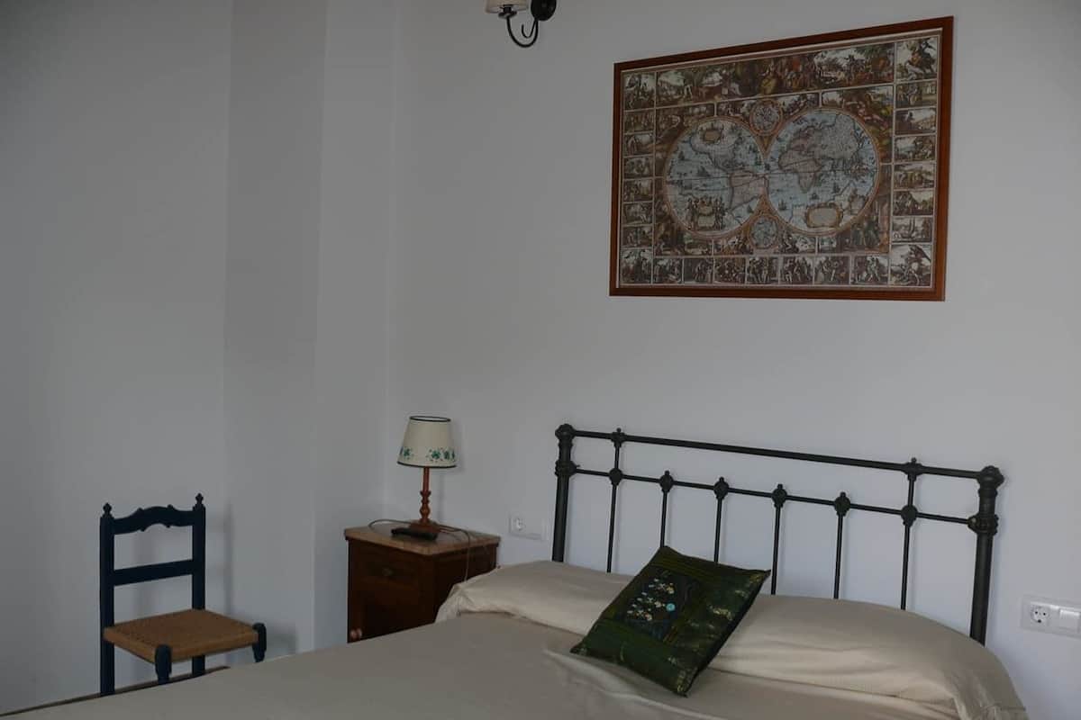 A bedroom with a bed, a chair, a nightstand, and a wall-mounted lamp.