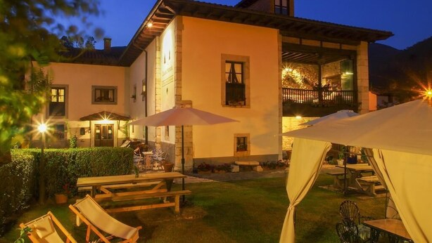 A well-lit outdoor area with a dining table, chairs, and umbrellas, suggesting a restaurant or dining area. - Casa de la Montaña (Onis)