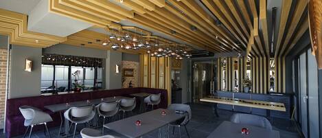 A modern restaurant with a unique ceiling design, multiple seating areas, and a bar.