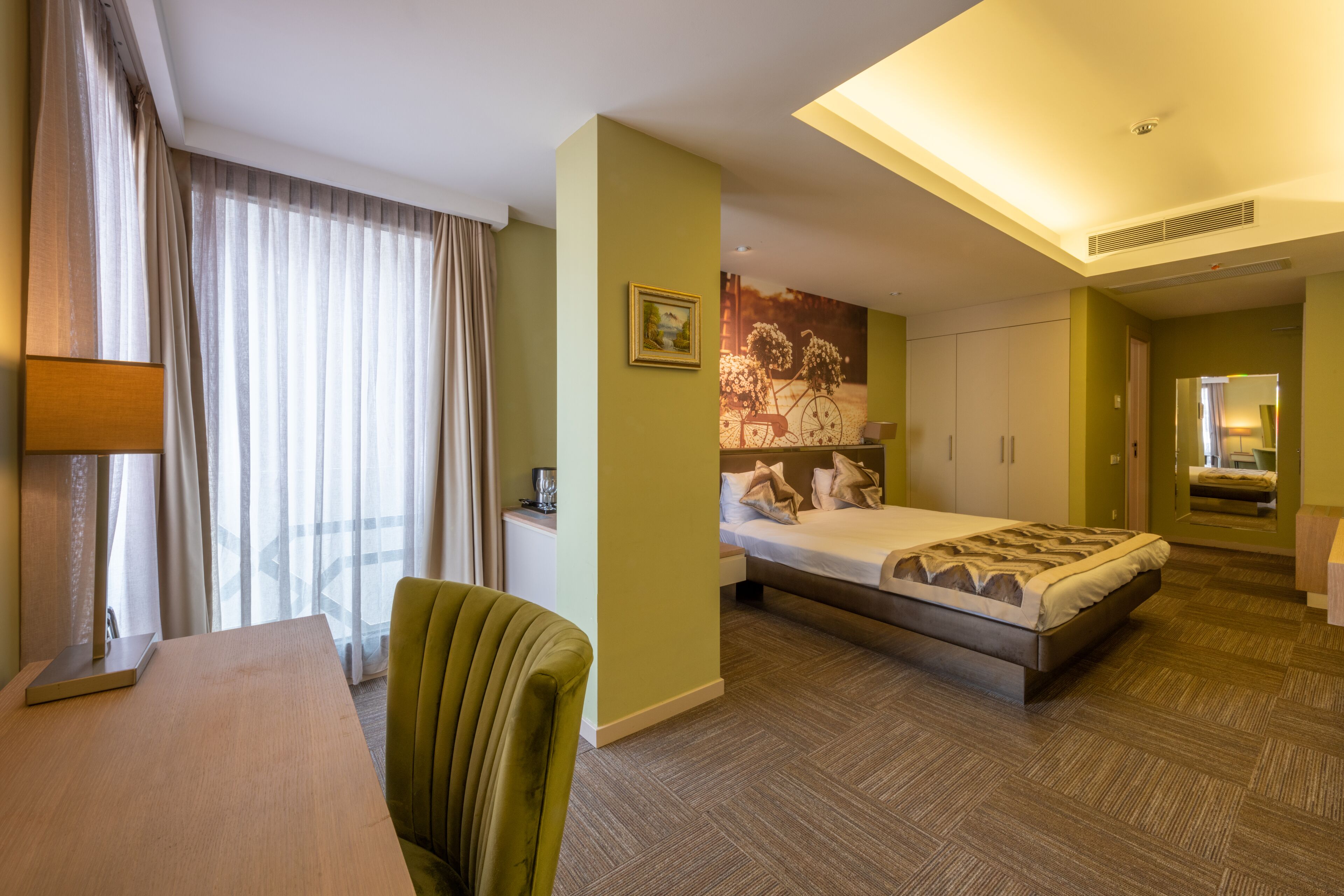 A hotel room with a bed, desk, chair, and a large window with curtains.
