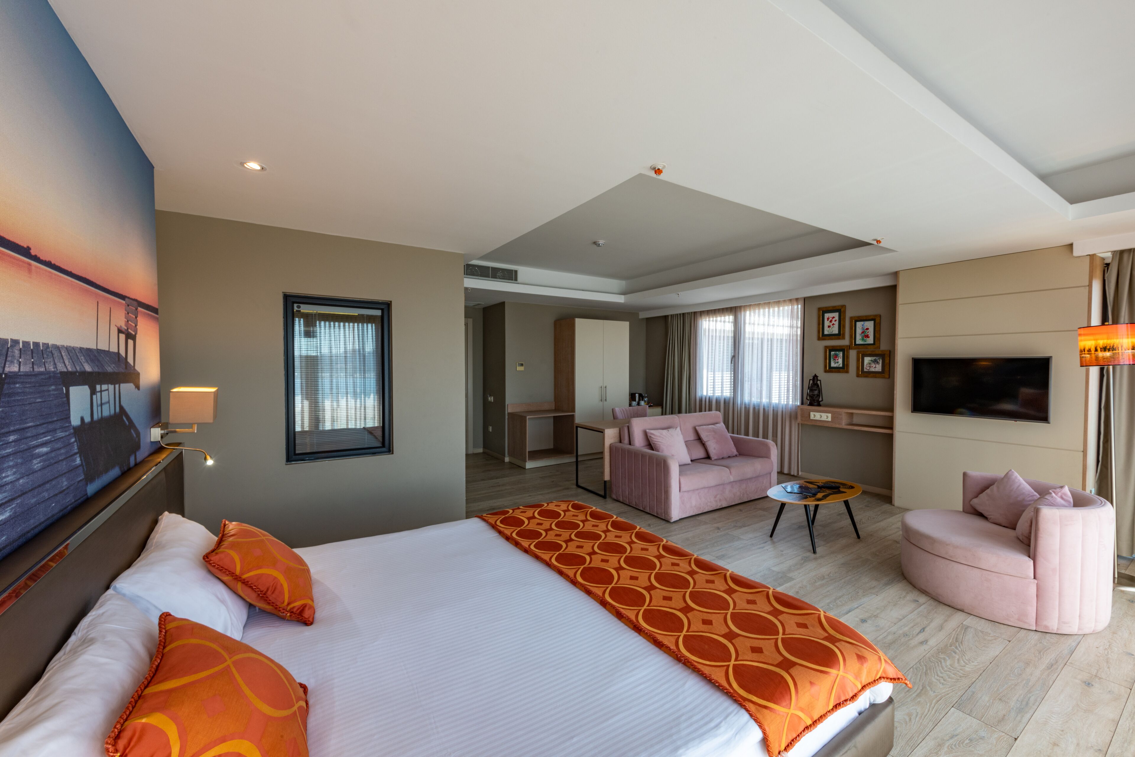 A hotel room with a large bed, two seating areas, a TV, and a view of the outside.