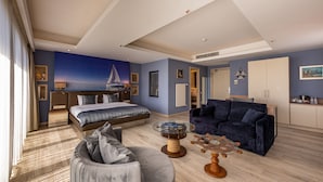 Une chambre d’hôtel moderne, équipée d’un lit, d’un canapé, d’une table basse en verre et offrant une vue sur la mer.