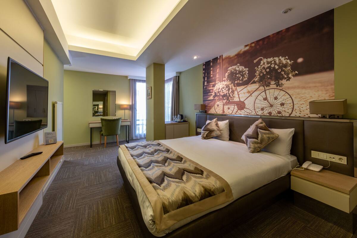 A modern hotel room with a large bed, a desk, a TV, and a wall-mounted phone.