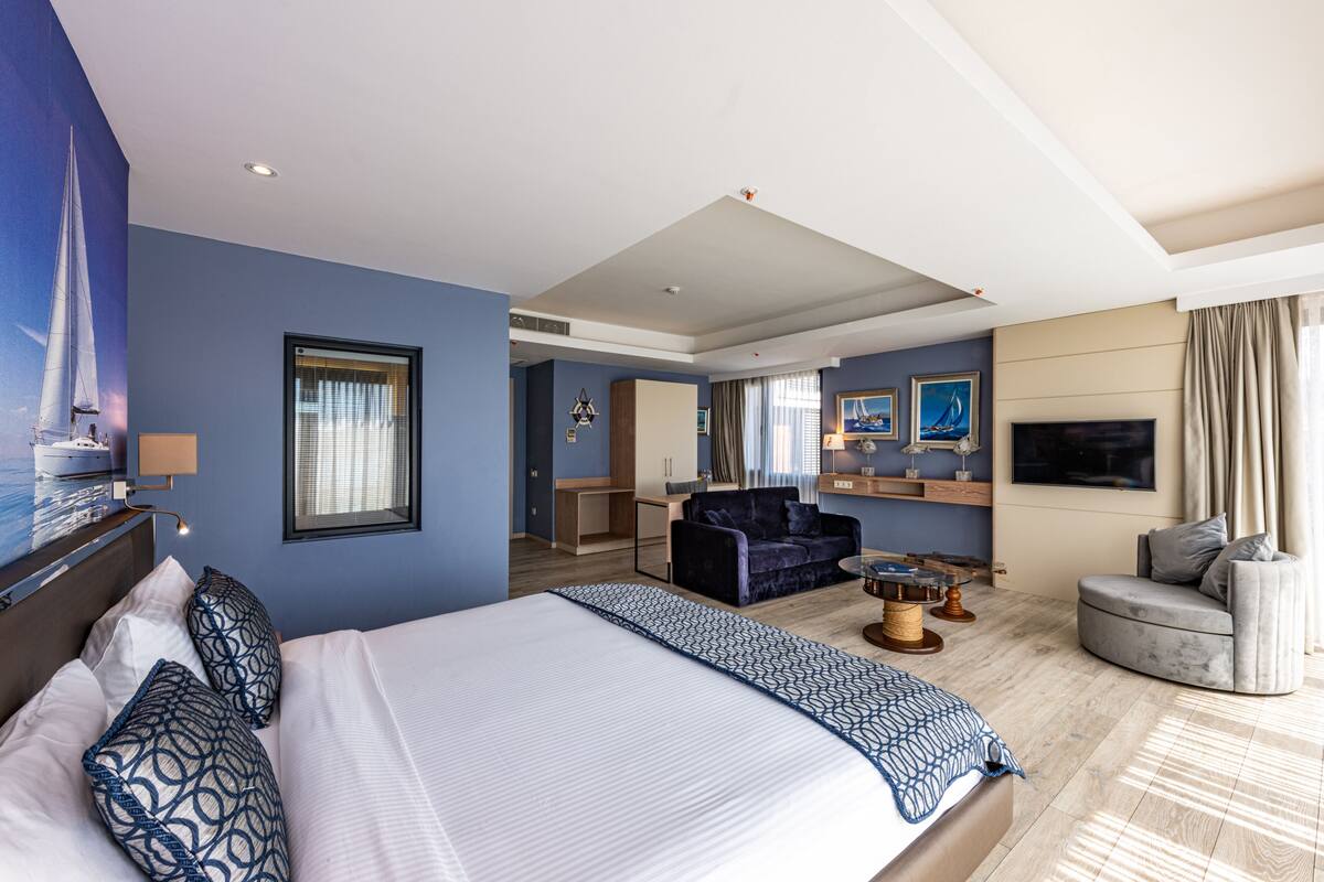 A modern hotel room with a large bed, a sofa, a TV, and a dining area.