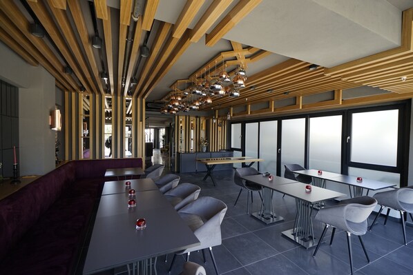 A modern dining area with wooden beams, pendant lighting, and a mix of seating arrangements including tables and a sofa.